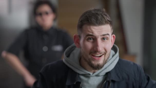 Young brunette Caucasian man with green eyes looking at camera talking as blurred police officer shaking head at background. Portrait of unfortunate burglar persuading innocence. — Stock Video