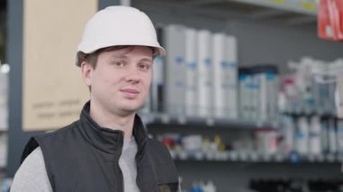 Arkaplanda bulanık raflarla hırdavatçıda poz veren genç beyaz adamın yakın plan portresi. Mutlu işçi gülümseyen kameraya bakıyor. Hizmet ve Meslek.