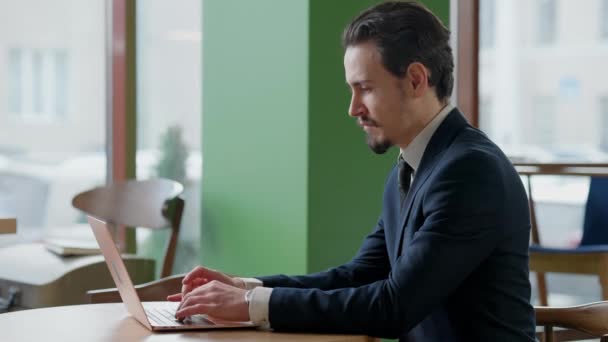 Widok z boku skoncentrowany biały mężczyzna z wąsami wpisując na klawiaturze laptopa wiadomości online. Pewny siebie skoncentrowany biznesmen w formalnym garniturze surfing Internet siedzi w kawiarni lub restauracji. — Wideo stockowe