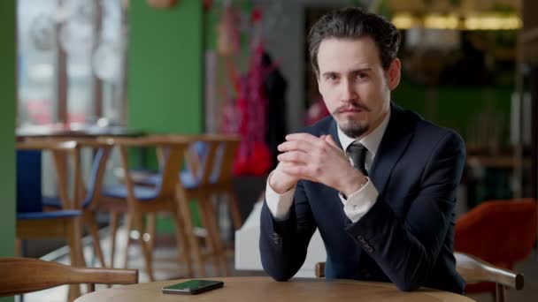 Retrato de hombre barbudo confiado con bigote sentado en la cafetería mirando la cámara. Guapo hombre de negocios caucásico en traje formal posando en la mesa en el restaurante interior. — Vídeos de Stock