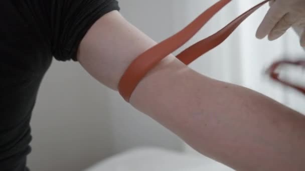 Close-up de mãos em luvas apertando arnês na mão de doador de sangue no hospital. Enfermeira irreconhecível ou médico preparando voluntário caucasiano doando na clínica. — Vídeo de Stock