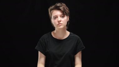 Kahverengi gözlü, zayıf esmer bir kadın kameraya ciddi bir yüz ifadesiyle bakmıyor. Siyah arka planda poz veren kendine güvenen beyaz kadın portresi.