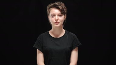 Kendinden emin gülümseyen esmer kadının portresi. Kameraya bakıyor ve güçlü bir hareket gösteriyor. Siyah arka planda poz veren ince beyaz kadın. Kadınlık ve güven kavramı.