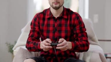 Genç, tanınmayan sakallı adam içeride oyun kumandası kullanıyor. Evde video oyunu oynayan konsantre olmuş beyaz erkek oyuncu var. Rekabet ve eğlence kavramı.