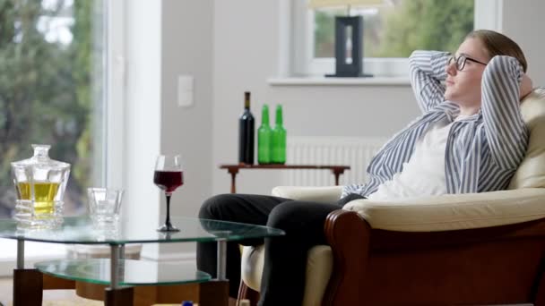 Seitenansicht eines depressiven jungen Mannes, der mit dem Kopf in den Händen auf einer Couch sitzt und Alkohol auf dem Tisch trinkt. Frustrierte süchtige kaukasische männliche Alkoholiker denken zu Hause drinnen. Alkoholproblem. — Stockvideo