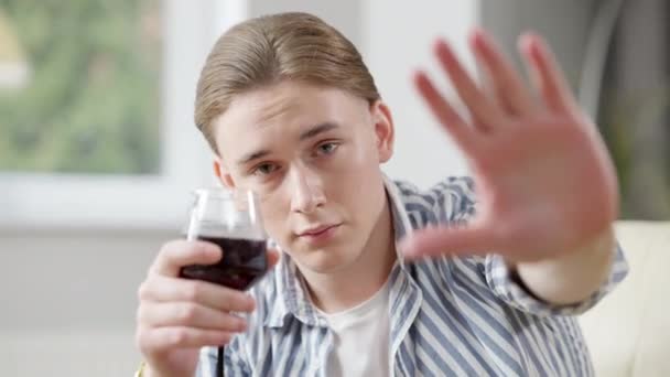 Mladý kavkazský pohledný muž natahuje dlaň, dívá se do kamery a drží sklenici s červeným vínem. Detailní portrét závislého alkoholika, jak dělá stop gesto. Závislák odmítá pomoc. — Stock video