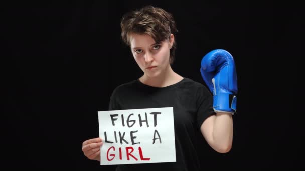 Magabiztos, komoly nő bokszkesztyűben, aki úgy küzd, mint egy lány, aki a kamerába néz. Portré magabiztos kaukázusi női aktivistáról, aki egyenlő emberi jogokért harcol, fekete alapon pózolva. — Stock videók