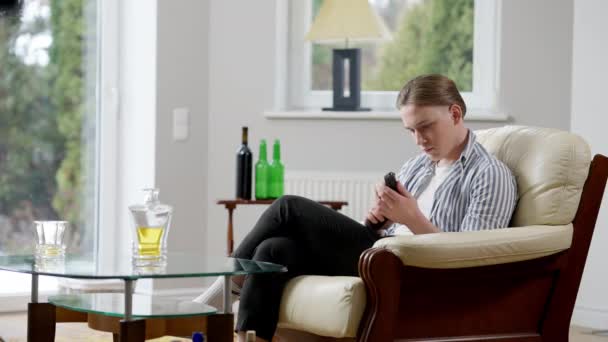 Gros plan de jeune homme déprimé avec un pistolet assis sur un fauteuil avec de l'alcool sur la table. Portrait latéral de la pensée alcoolique masculine caucasienne frustrée sur le suicide. Concept de crise et de dépendance. — Video