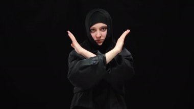 El ele tutuşan tesettürlü genç bir kadın kameraya ciddi bir yüz ifadesiyle bakmıyor. Siyah arka planda zorbalık ve aşağılanma kurbanı ezilen Müslümanların portresi.