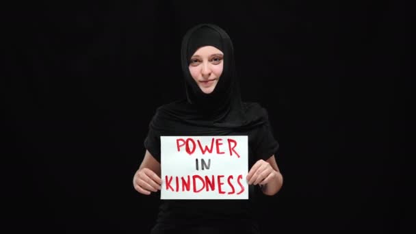 Retrato de mulher muçulmana sorridente em hijab segurando Power em sinal de bondade olhando para a câmera. Positivo confiante jovem posando no fundo preto. Igualdade de género e conceito de direitos humanos. — Vídeo de Stock