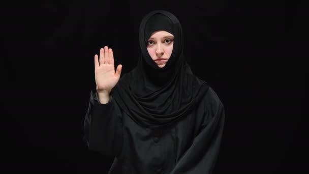 Foto en medio de una deprimida mujer musulmana aterrorizada levantando la palma con el pulgar mirando a la cámara. Retrato de víctima oprimida de violencia doméstica posando en un fondo negro mostrando un signo para ayudar. — Vídeos de Stock