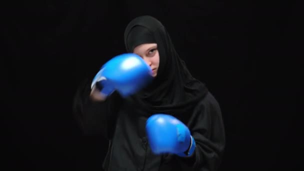 Soustředěná sebevědomá muslimka boxující kameru s rozzlobeným výrazem obličeje. Portrét mladé boxerky v rukavicích pózujících na černém pozadí. Rovnost v bojových uměních a lidských právech. — Stock video