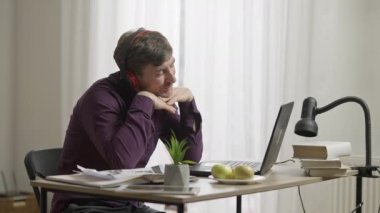 Yakışıklı, mutlu bir adam online randevularda görüntülü sohbet yapıyor. Kulaklıklı romantik gülümseyen beyaz adamın yan görüntüsü. Laptop ekranına hava öpücüğü yolluyor..