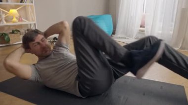 Canlı kamera, konsantre sporcu karın kaslarını çalıştırıyor oturma odasında egzersiz minderinde yatıyor. Evde çalışan yakışıklı, beyaz tenli bir adamın portresi. Sportif yaşam tarzı.