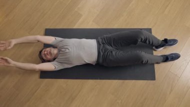 Kafkasyalı orta yaşlı bir adamın spor yaptıktan sonra spor minderinin üzerinde yattığını gösteren geniş bir görüntü. Evde antrenman yaptıktan sonra dinlenen yakışıklı sporcunun portresi. Spor ve yaşam tarzı.