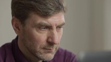 Laptop ekranına bakan odaklanmış adamın görüntüsü. Orta yaşlı beyaz adam internette sörf yapıyor, sosyal medyayı kullanıyor ya da evde online film izliyor. Yaşam tarzı ve teknolojileri.