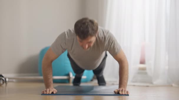 Visão frontal de homem apto confiante fazendo flexões e olhando para a câmera sorrindo. retrato de esportista caucasiano de meia-idade positivo treinando em casa dentro de casa. Conceito de treino e desporto. — Vídeo de Stock