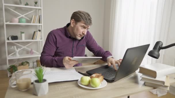 Retrato de um homem ocupado falando ao telefone, usando laptop e tablet, e escrevendo notas. Excesso de trabalho homem de negócios caucasiano ou empregado que trabalha em casa dentro de casa. Conceito de estilo de vida empresarial. — Vídeo de Stock