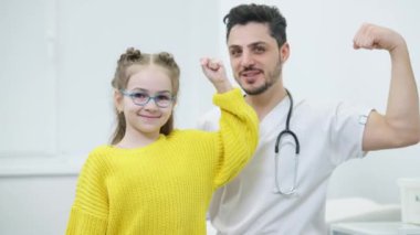 Gözlüklü mutlu beyaz kız ve kameraya bakarak güç gösterisi yapan Orta Doğulu adam. Hastanenin içinde poz veren neşeli doktor ve hasta portresi. Sağlık hizmeti kavramı.