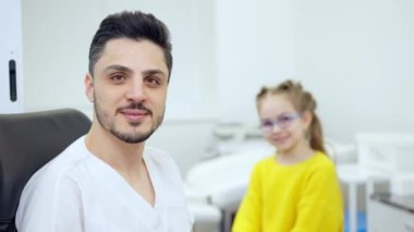 Arka planda bulanık beyaz bir kızla hastanede poz veren kendinden emin Orta Doğulu çocuk doktoru portresi. Pozitif yakışıklı adam kameraya bakıyor gülümseyen danışman hasta.