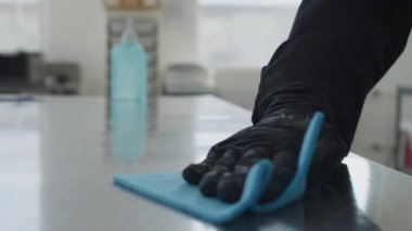 Mutfakta dezenfektan ve siyah eldiven temizleme masasında kadın elinin yakın çekimi. Tanımlanamayan bir kadın iş yerini dezenfekte ediyor. Covid-19 salgınında yeni normal çalışma.