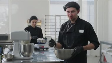 Kafkas 'lı genç bir adamın arka planda yumurta tartan bulanık kadın pozu. İş yerinde tatlı malzemeleriyle gülümseyen pozitif bir fırıncı. İş ve aşçılık..