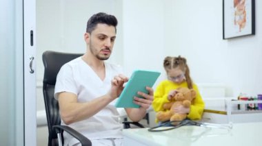 Arka planda oyuncak ayıyla oynayan bulanık bir kız gibi tablet kullanan konsantre olmuş yakışıklı bir çocuk doktoru. Kafkas hastalarını tedavi eden ciddi bir Orta Doğulu adamın portresi..
