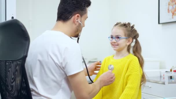 Portret van een charmant blank meisje dat inhaleert en uitademt als arts met stethoscoop. Leuke kleine patiënt die een bezoek brengt aan de Midden-Oosterse arts kinderarts in het ziekenhuis. Medisch onderzoek. — Stockvideo