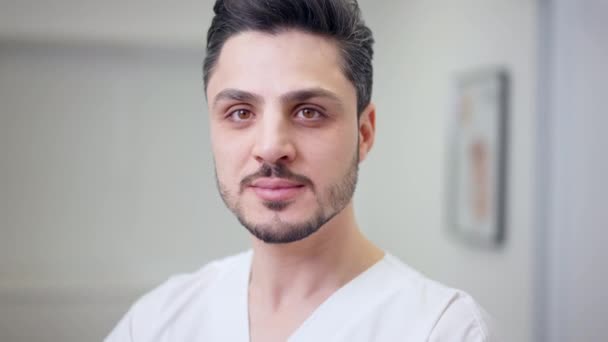 Headshot of handsome young Middle Eastern doctor with brown eyes looking at camera smiling. Close-up portrait of confident male physician posing in hospital indoors. — Stock Video