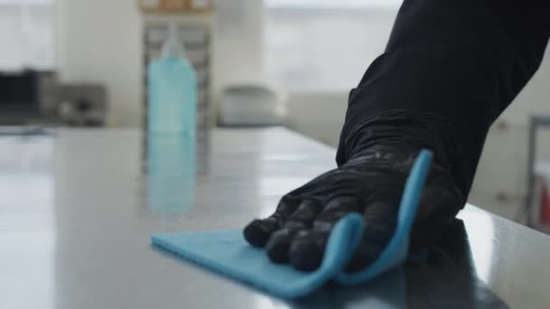 Zbliżenie żeńskiej dłoni w czarnej rękawicy stół czyszczący ze środkiem dezynfekującym w kuchni. Nierozpoznawalna kobieta dezynfekująca miejsce pracy środkiem dezynfekującym. Nowe normalne prace nad pandemią Covid-19. — Wideo stockowe