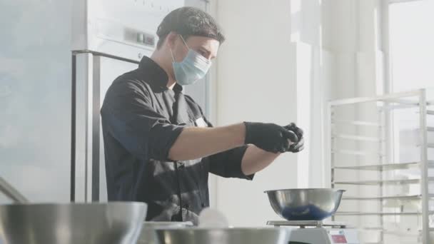 Portret środkowego ujęcia skoncentrowanego cukiernika bijącego jajka na ciasto w zwolnionym tempie w słonecznej kuchni. Profesjonalny mężczyzna rasy kaukaskiej w masce Covid-19 pracujący w sklepie ze słodyczami. — Wideo stockowe