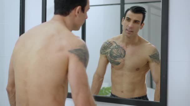 Reflection in bathroom mirror of confident handsome man admiring himself. Portrait of tattooed Middle Eastern narcissistic guy at home in the morning. Lifestyle and confidence concept. — Stock videók