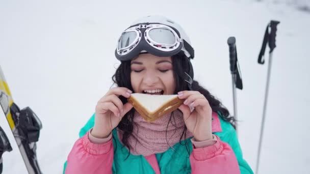 Portret szczęśliwej kobiety delektującej się smaczną kanapką w ośrodku zimowym na świeżym powietrzu. Wesoła biała turystka jedząca przekąski. Koncepcja odpoczynku i turystyki. — Wideo stockowe