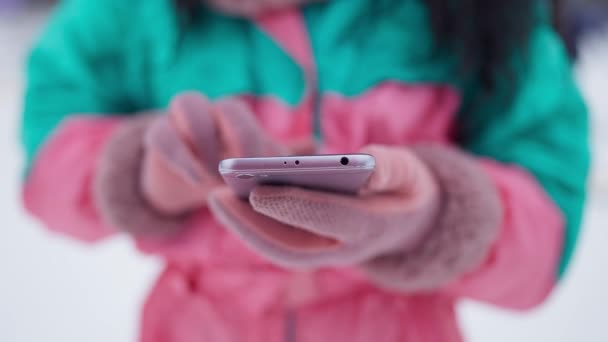 Primer plano del teléfono inteligente en manos femeninas al aire libre. Mujer irreconocible en traje de esquí y manoplas rosas mensajería en línea descansando en la estación de invierno. Comunicación inalámbrica y vacaciones de invierno. — Vídeos de Stock