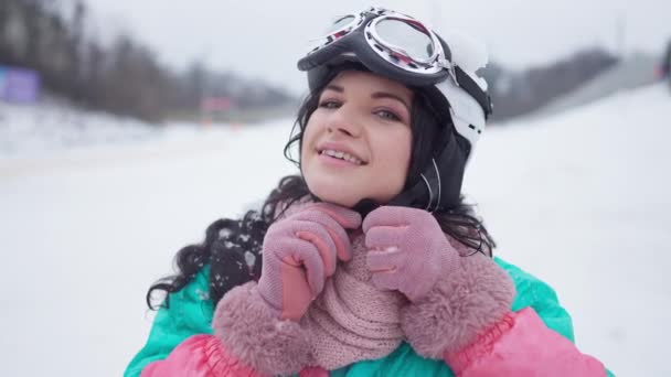 Heureux skieur féminin satisfait décoller casque de ski en regardant la caméra souriant. Joyeux Caucasien belle femme posant à la station d'hiver après le ski en plein air. — Video