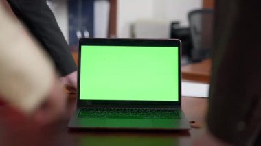 Etrafta tanınmayan iş adamları olan yeşil ekranlı dizüstü bilgisayara yakın çekim. Ofiste Chromakey cihazı var. İnternette analiz yapan kadın ve erkekler var. Modern teknolojiler ve e-ticaret.