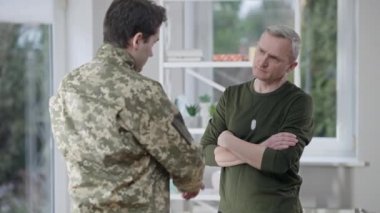 Yoğunlaşmış gri saçlı baba yetişkin oğullarına bakıyor kamuflaj yapıyor ve omuzlarını okşuyor. Beyaz gururlu orta yaşlı bir adamın portresi askerin gitmeye hazırlanmasına yardım ediyor..