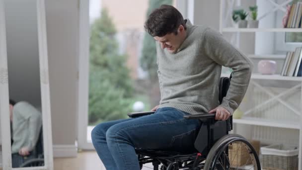Knappe, geconcentreerde jonge verlamde man met verlamde benen die probeert binnen in een rolstoel op te staan. Portret van een zelfverzekerde blanke invalide die herstelt na een trauma. Inspanningen en geneeskunde. — Stockvideo