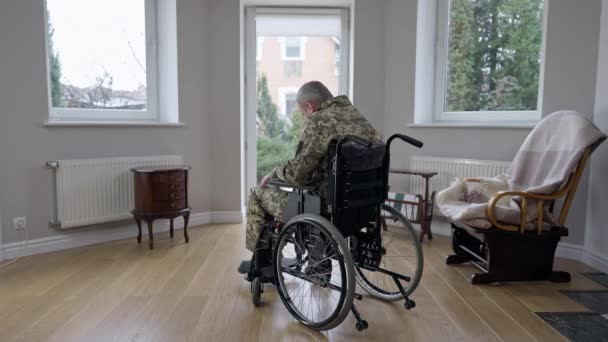 Visão ampla de costas de veterano militar motivado de cabelos grisalhos tentando se levantar da cadeira de rodas. Homem caucasiano paraplégico fazendo esforços para a recuperação em casa dentro de casa. Paralisia médica e incapacidade. — Vídeo de Stock