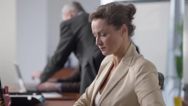 Side view portrait of busy focused confident woman working in office with blurred colleagues at background. Concentrated beautiful slim Caucasian employee analyzing statistics indoors. — Stock Video