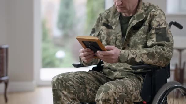 Veterano irreconocible de mediana edad en uniforme militar en silla de ruedas mirando fotografía y llorando. Soldado caucásico sin esperanza con trastorno de estrés postraumático en casa en interiores. — Vídeos de Stock