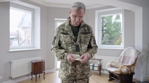 Ritratto di un triste soldato di mezza età che tiene soldi e pensa. Uomo militare caucasico frustrato in piedi in casa con contanti. Servizio e stile di vita. — Video Stock