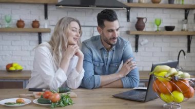 Genç, ırklar arası bir çift mutfakta görüntülü konuşma yapıyor. Güzel beyaz kadın ve yakışıklı Orta Doğulu adam içeride dizüstü bilgisayarla konuşuyor ve gülümsüyor. Milenyum yaşam tarzı.