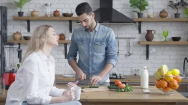 Yakışıklı Orta Doğulu adam sağlıklı salata için salatalık kesiyor ve güzel beyaz bir kadınla mutfakta tartışıyor. Evde eşiyle kavga eden sinirli koca portresi..