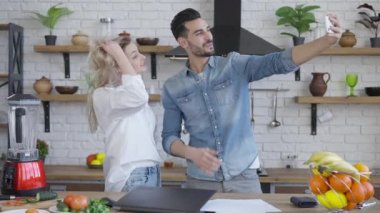 Mutlu zengin milenyum çifti evde mutfakta selfie çekiyor. Kendine güvenen yakışıklı Orta Doğulu bir adam ve içeride fotoğraf çeken güzel beyaz bir kadın. Zenginlik ve yaşam tarzı.