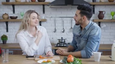 Mutfakta konuşan ve gülümseyen ırklar arası genç bir çift. Mutlu Kafkasyalı kadın ve Orta Doğulu erkek hafta sonu evde eğleniyor. İlişki ve mutluluk.