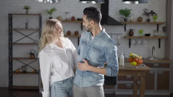 Heureux couple interracial amoureux posant dans la cuisine à la maison. Belle femme blonde blanche mince et beau homme confiant Moyen-Orient regardant caméra étreignant et souriant. Amour et unité. — Video