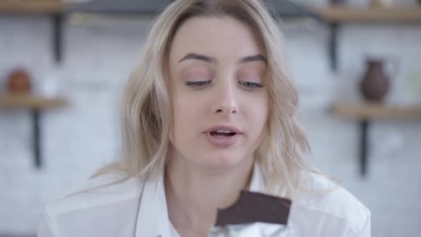 집안에서 초콜릿 바를 먹는 슬픈 금발 여성의 근접 사진. 우울해 하는 백인 여성 이 부엌에서 맛있는 달콤 한 디저트를 무고 씹는 모습. — 비디오