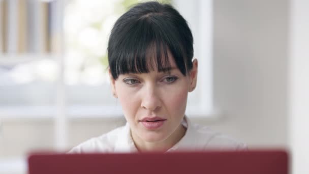 Headshot de concentrat pozitiv femeie încrezător mesagerie on-line uitându-se la ecranul laptop. Portret apropiat al unei tinere femei de afaceri caucaziene concentrate în birou în interior. Stil de viață și succes . — Videoclip de stoc