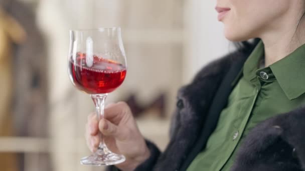 Copa de vino tinto en mano delgada femenina de cerca. Mujer joven caucásica irreconocible sacudiendo y degustando deliciosa bebida de lujo en el interior. Concepto de riqueza y lujo. — Vídeos de Stock